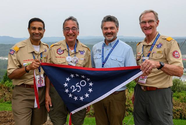 Devang Desai, Ricky Mason, Peter Churchbourne and Roger Krone display the Great American Expedition flag at the 2026 National Scout Jamboree